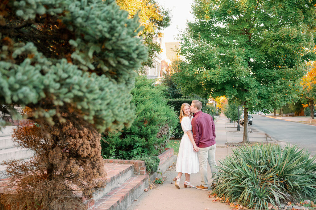 Couple kisses on Monument Ave sidewalk, engagement photo outfits for fall, burgundy and white engagement photos, Richmond couple